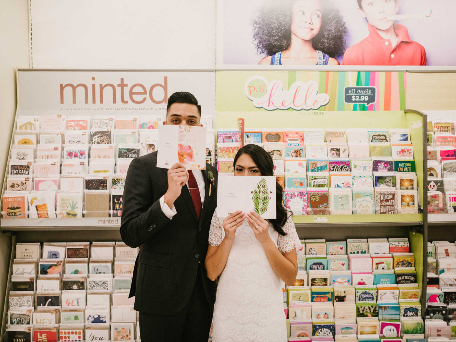 Bride and groom stand in card aisle of Target holding up cards so only part of their face shown are their eyes