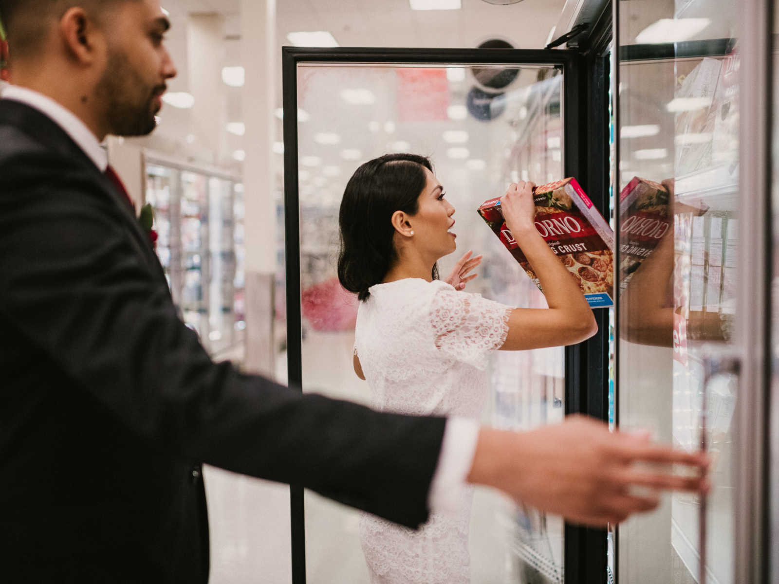 Groom looks over to see his bride grabbing a box of frozen pizza from freezer aisle at Target