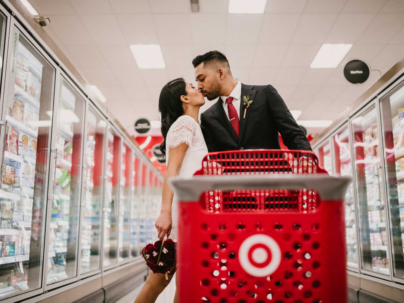 Bride and groom kiss in freezer aisle of Target while groom holds on to shopping cart