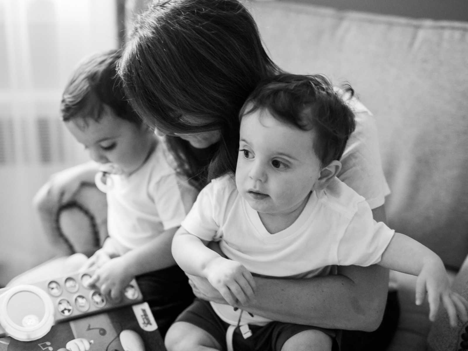 Mother sits in chair holding toddler twins that were conceived through IVF in her lap