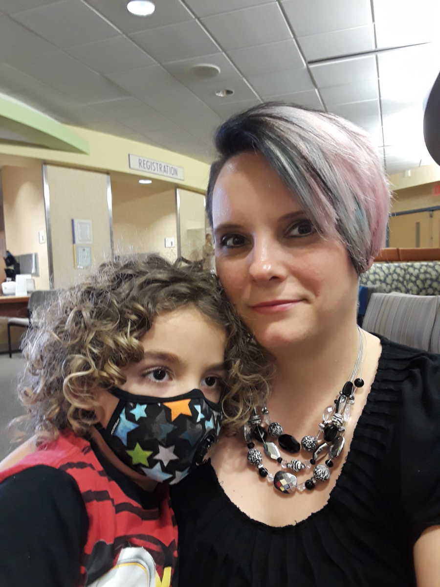 Mother smiles in selfie with son with leukemia in doctors waiting room
