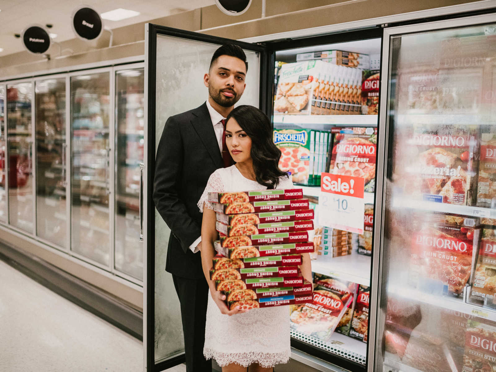 Bride and groom pose in front of freezer door while bride holds large stack of frozen pizza boxes at Target