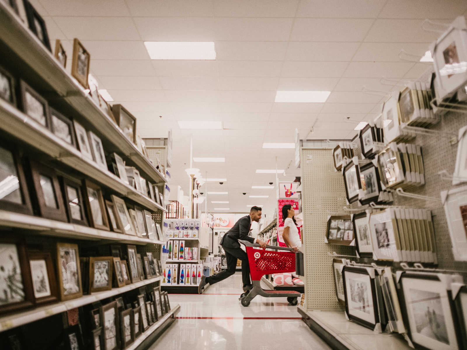 View from picture frame aisle in Target of groom pushing the shopping cart he and his bride are riding
