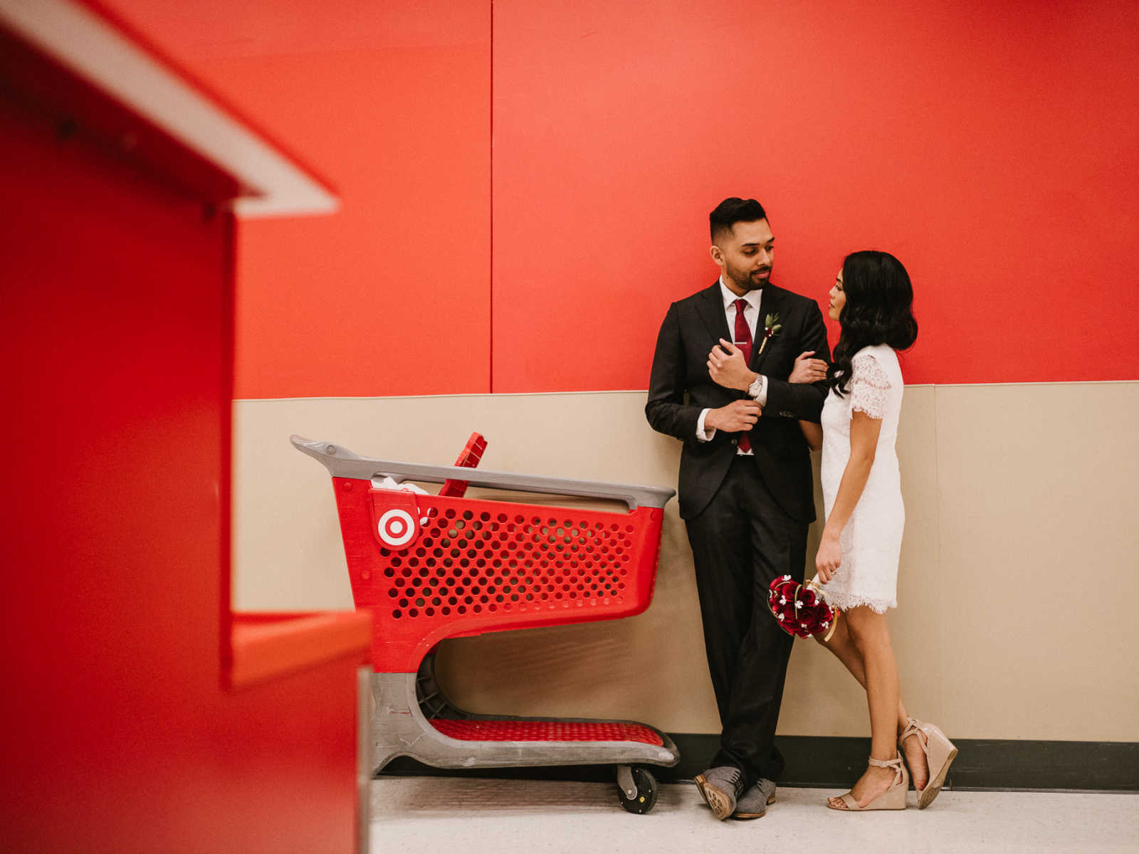 Bride and groom lean against a wall arm and arm staring into each others eyes next to Target shopping cart