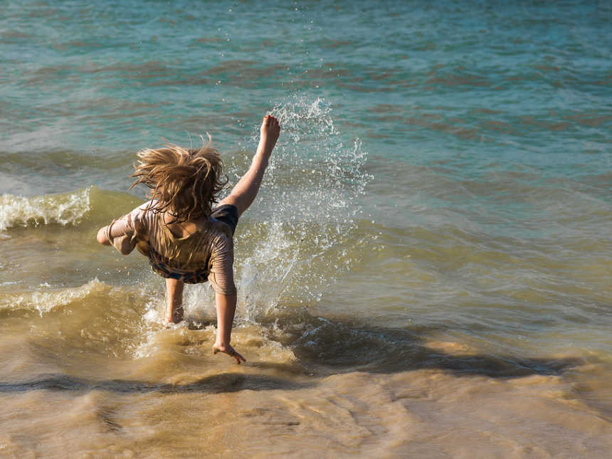 Boy in the middle of falling on his back in shallow body of water