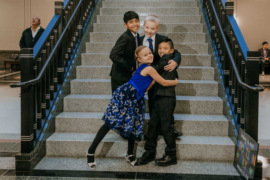 Birth son and daughter hug adopted brothers on stairs of adoption court