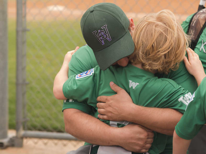 Father hugging young son after baseball game