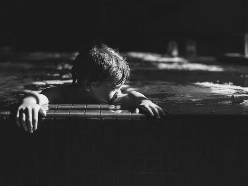 Young boy holding on to the side of the pool looking to his side in black and white