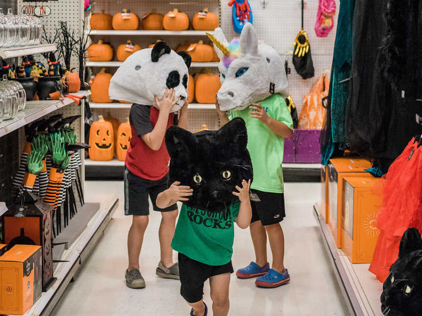 Boys in halloween aisle of store wearing a panda, cat, and unicorn mascot head