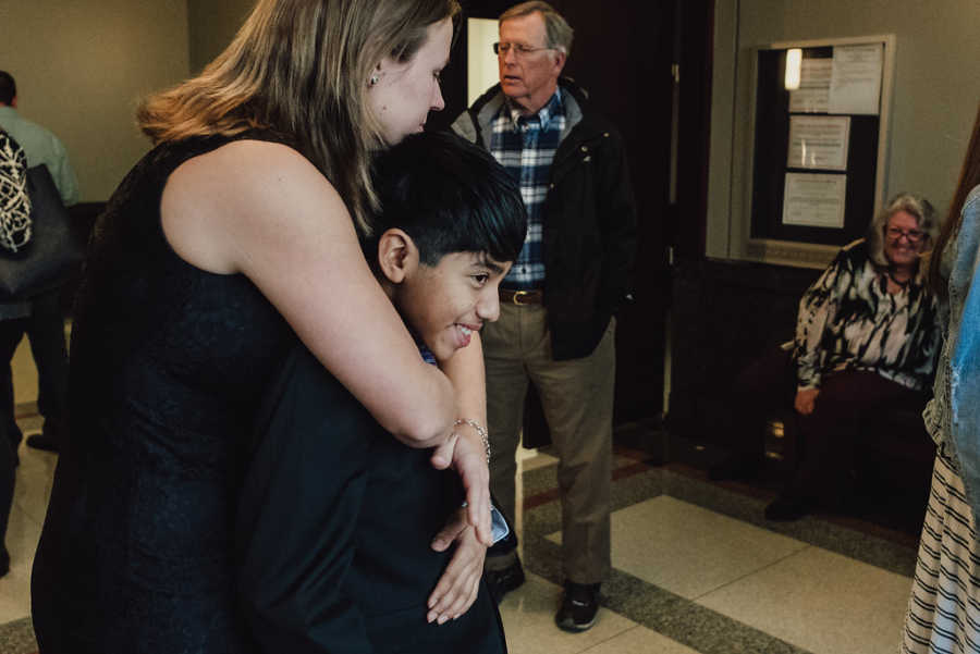 Mother hugs adopted son from behind in hall of adoption court