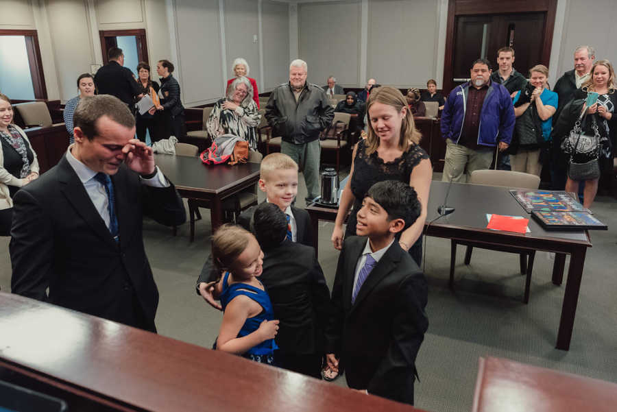 Adopted sons and birth children smile while father cries and mother watches at adoption court