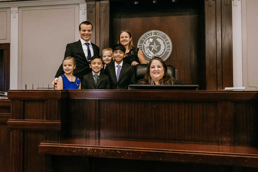 Mother and father of two adopted sons and two birth children smile at adoption court behind judge