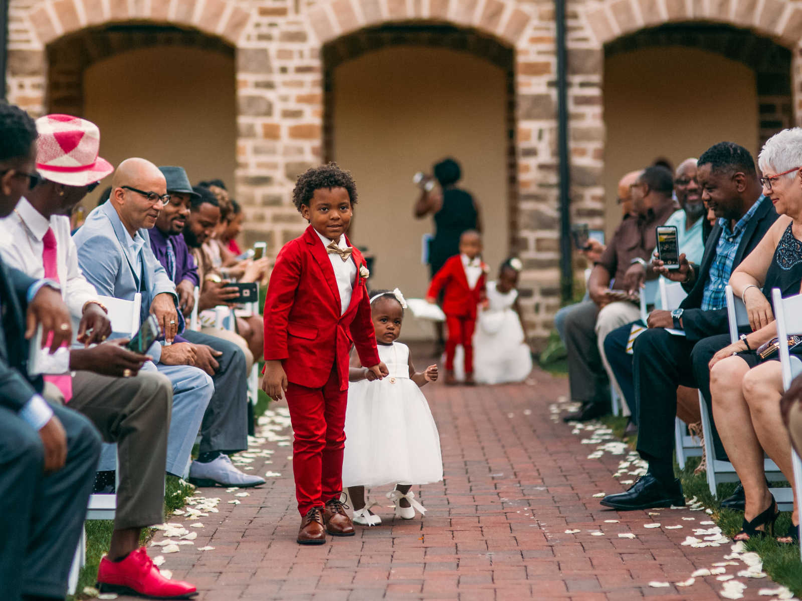 Son of bride smiles while walking down aisle holding hands with little girl in white dress