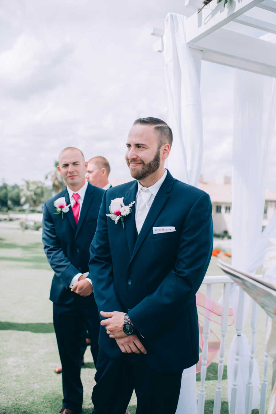 Groom smiles as he waits at altar of outdoor wedding
