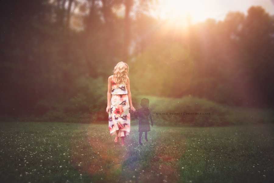 Woman who suffered miscarriage stands in field holding hands with shadow to represent lost child