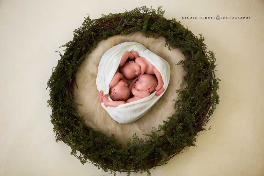 Triplets swaddled in blanket sleeping in circle surrounded by wreath
