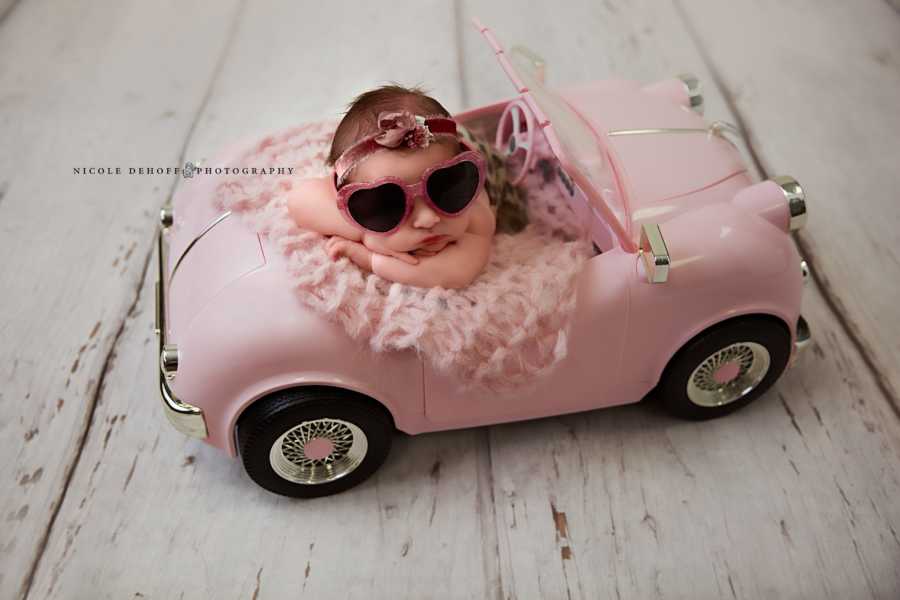 Newborn whose mother used sperm donor asleep in pink toy convertible with sunglasses on 