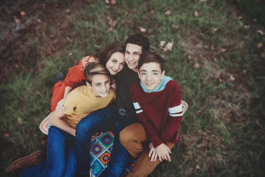 Three teen siblings sit in grass with their adopted brother looking up