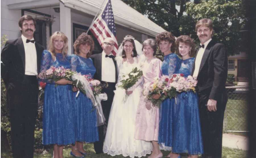 Bride stands beside mother and father and other family members at wedding wearing gown her mother made her