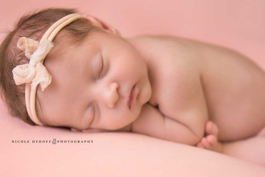Close up of newborn whose mother used a sperm donor asleep with tan headband with bow on it