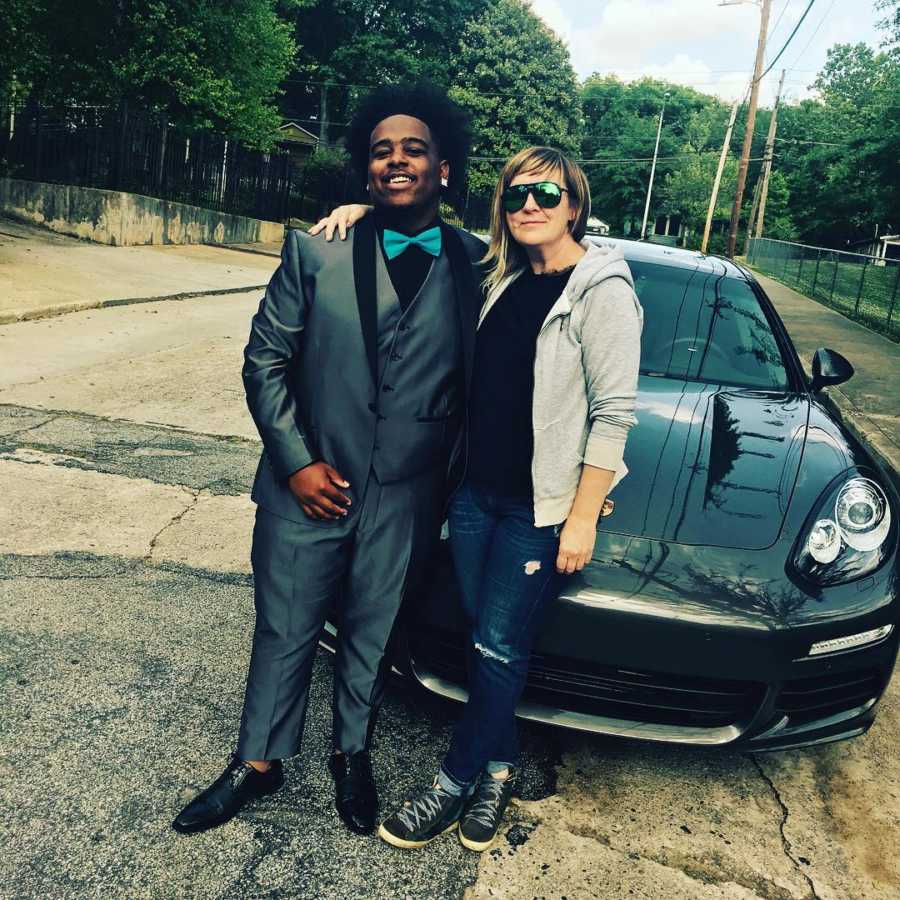 Woman who owns porsche and drives teen couple to prom stands smiling with boyfriend