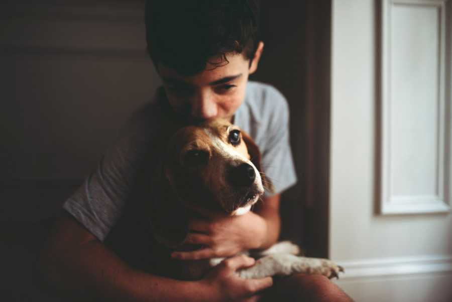 Boy adopted by teacher kisses dog on forehead who is sitting in his lap