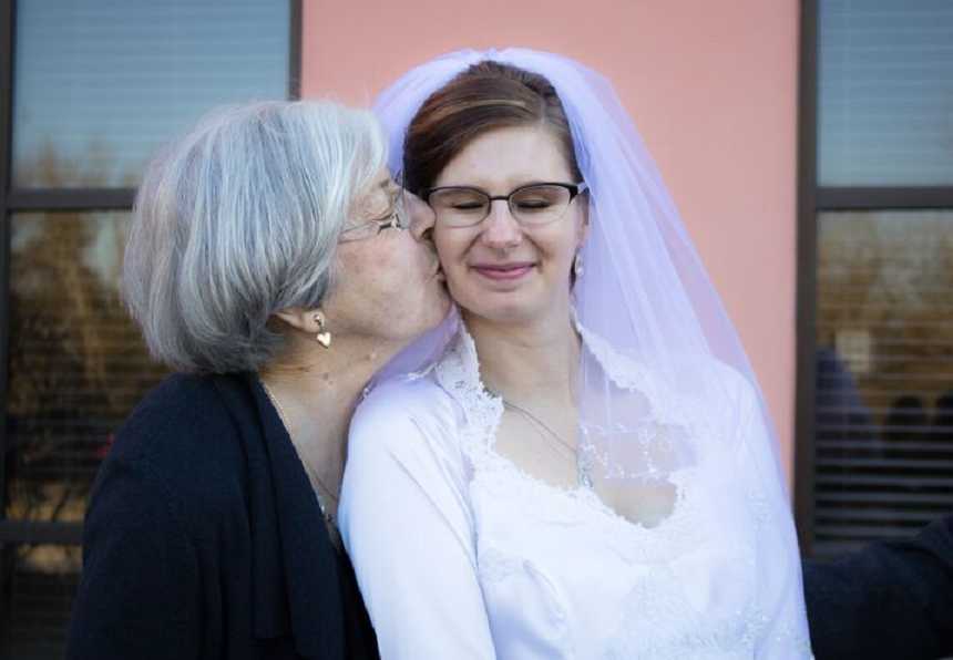 Grandmother kissing cheek of granddaughter who is wearing wedding gown she made
