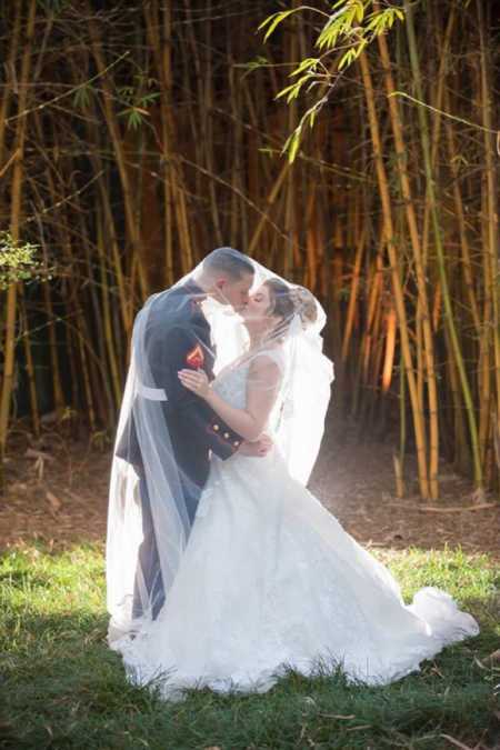Bride and soldier kissing on wedding day surrounded by veil