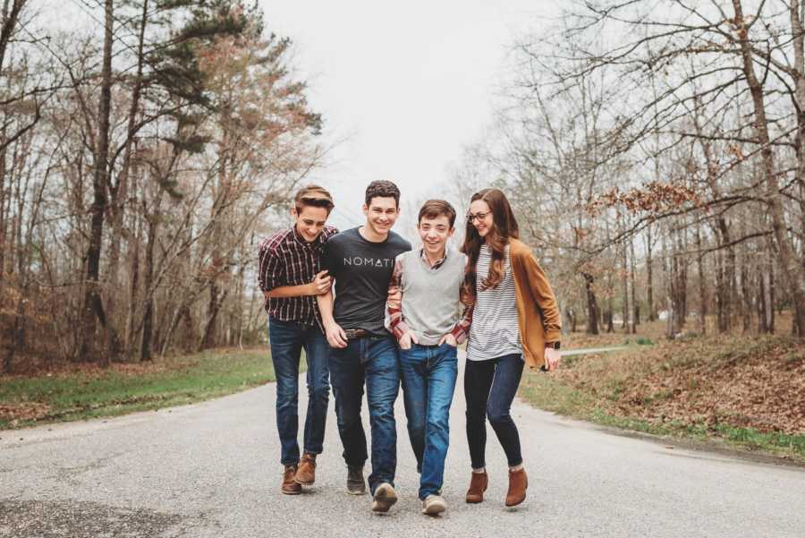 Three siblings walk arm in arm with their adopted brother down middle of street