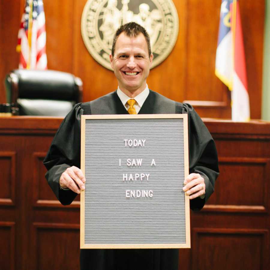 Judge in adoption court holding sign saying, "Today I saw a happy ending"