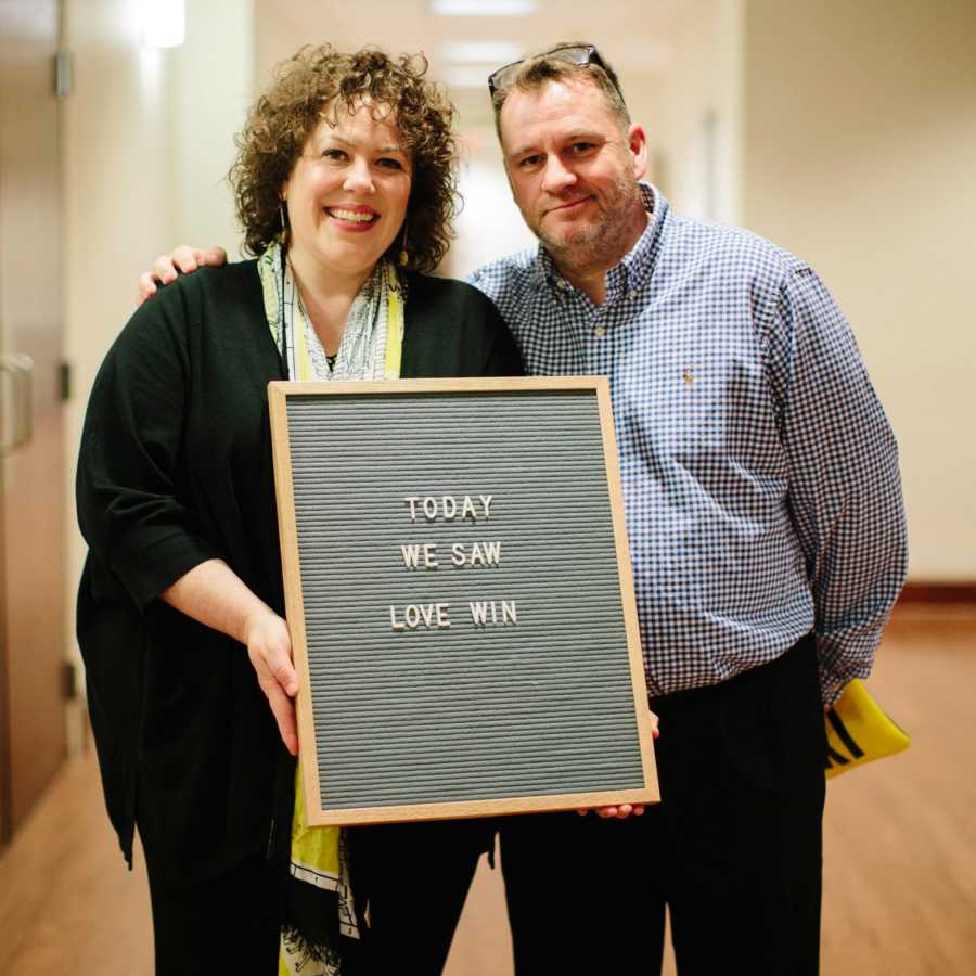 Man and woman at adoption court holding sign saying, "Today we saw love win"