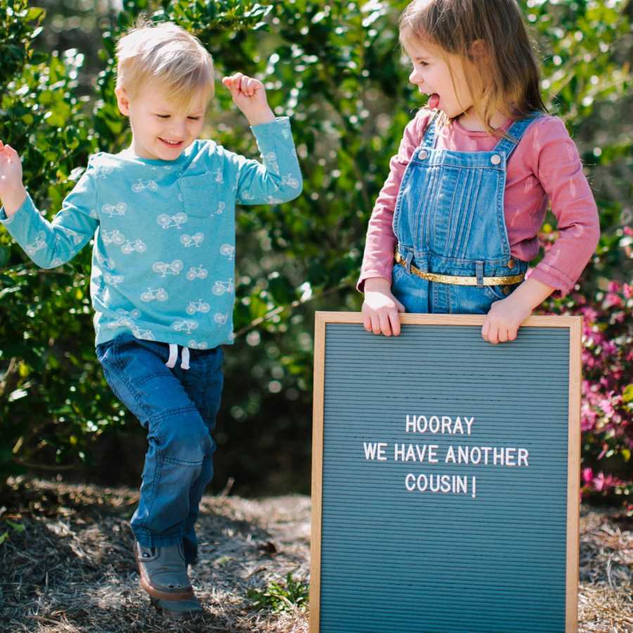 Cousins of adopted child stand outside holding sign saying, "Hooray we have another cousin"