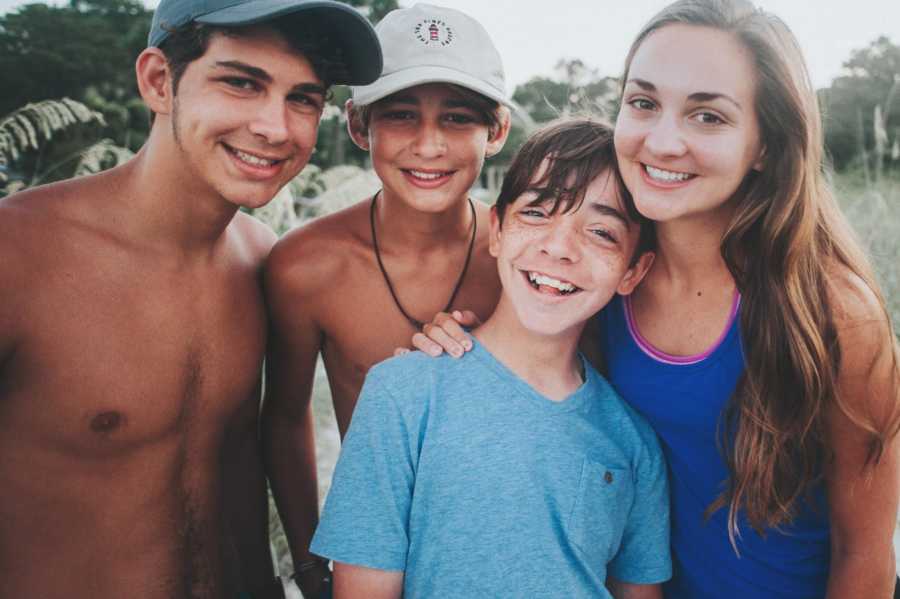 Three teens standing smiling behind adopted brother