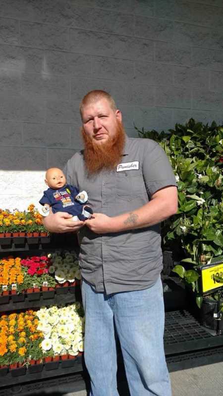 Man stands outside near flowers with daughter's baby doll in his arms