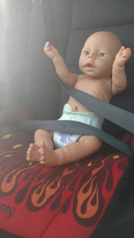 Baby doll sitting up in red flamed carseat with seat belt on