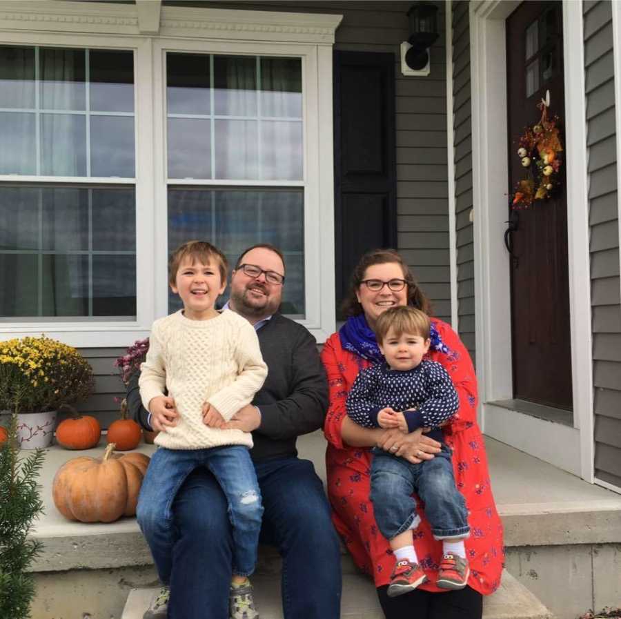 Adopted woman sits with her husband and two boys on their lap on front porch