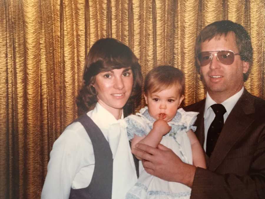 Husband and wife holding their adopted baby who has her finger in her mouth