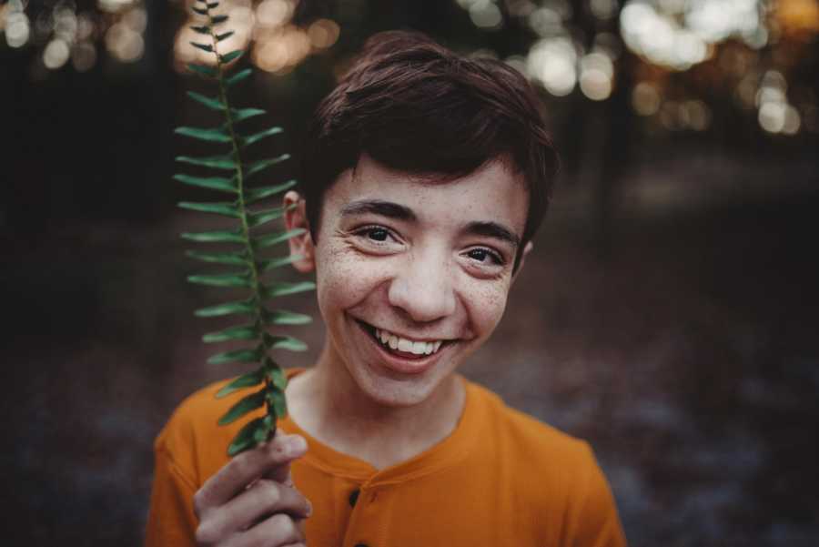 Boy who was adopted by teacher holds up leaf and smiles
