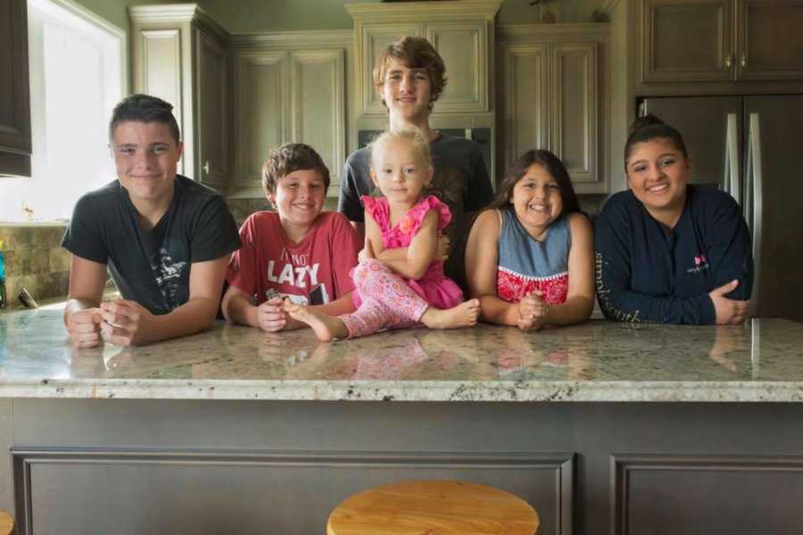 Birth child sitting on counter surrounded by 5 siblings who were adopted