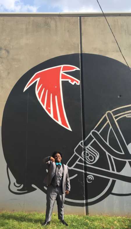 Teen standing in front of sign of Atlanta Falcon's helmet dressed for girlfriend's prom