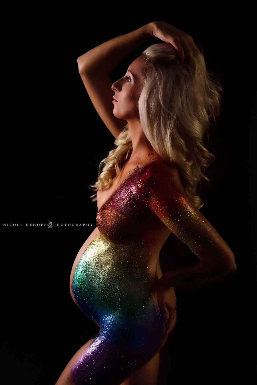 Pregnant woman poses with rainbow sparkles along side of her body 