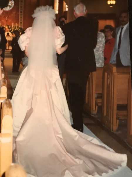 View of back of bride walking down aisle arm in arm with father in dress mother made for her