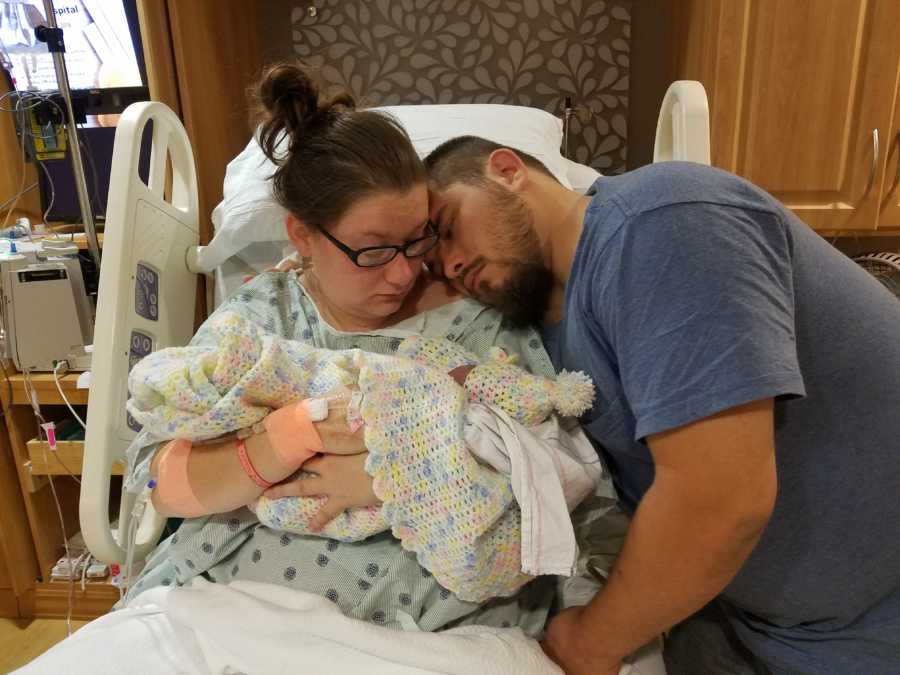 Woman who just gave birth holding her still born baby in her arms with husband resting head on her shoulder