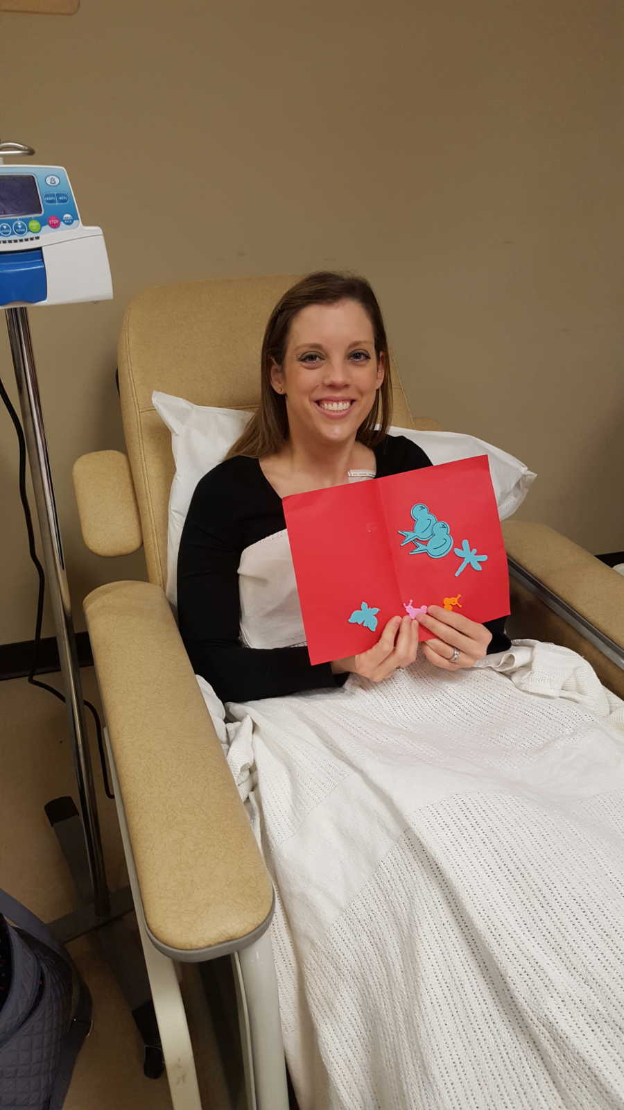 Mother with breast cancer sits in hospital chair holding handmade card
