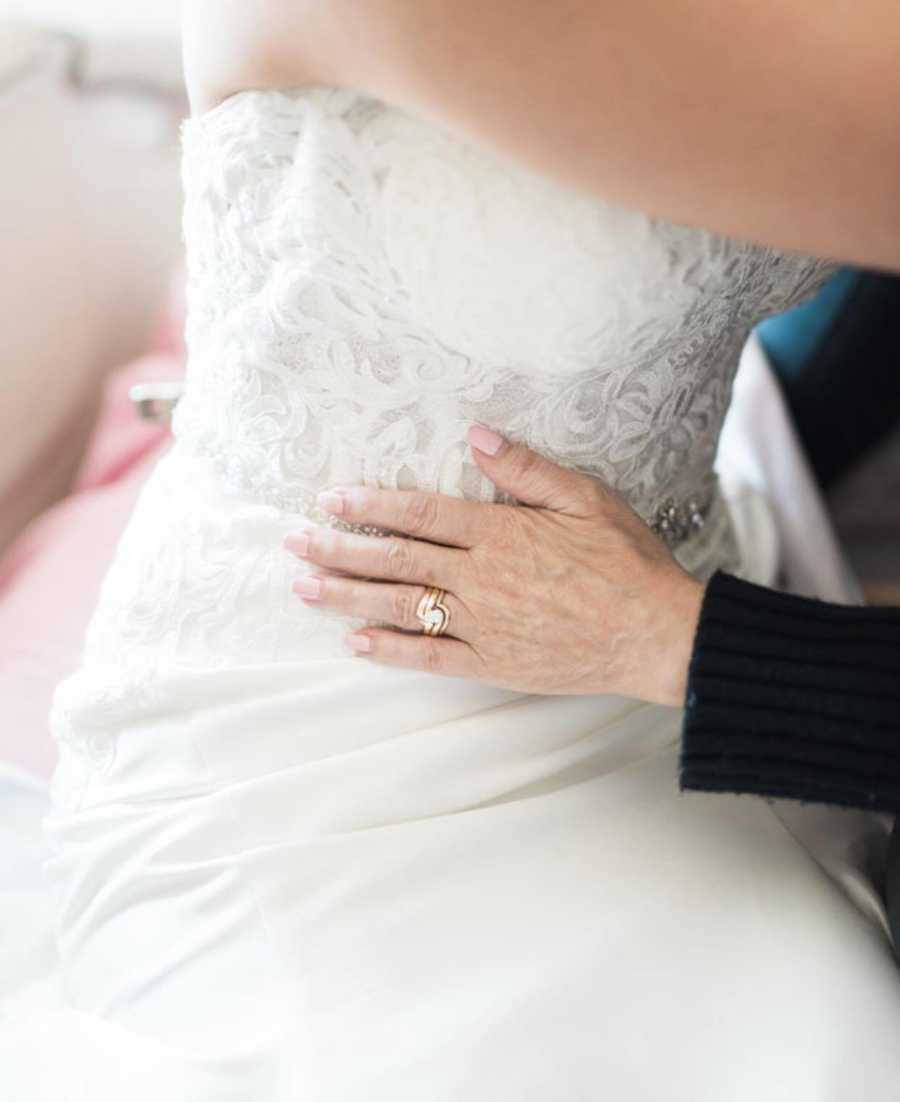 Close of up terminally ill woman's hand with wedding ring on daughters waist who is wearing wedding gown