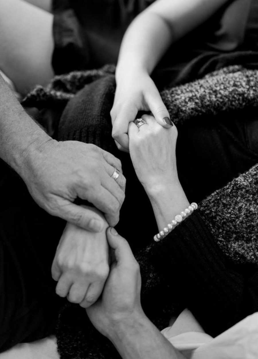 Close up of husband, daughter, and son holding terminally ill woman's hand