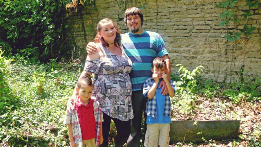 Pregnant mother who will have a stillborn baby smiling next to husband and two son's in front of her 