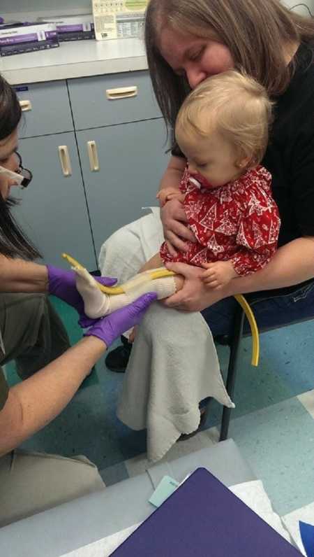 Mother holds newborn baby in her lap as she is fitted for a cast