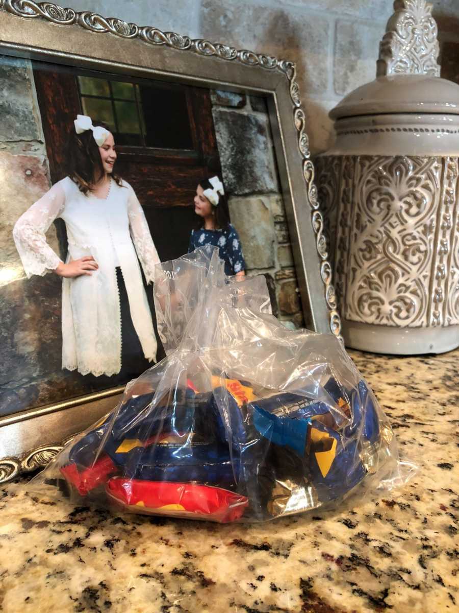 Clear bag of Halloween candy sitting on counter in front of picture frame of foster sisters holding hands
