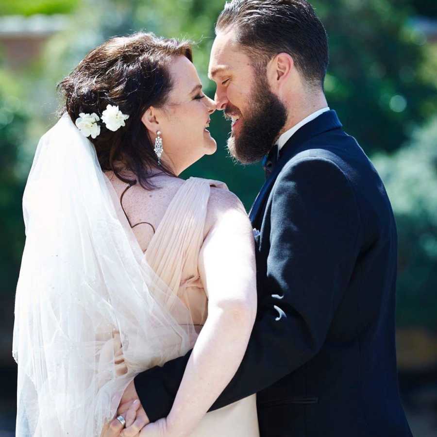 Husband and wife in wedding attire smiling at each other after losing combined 400 pounds